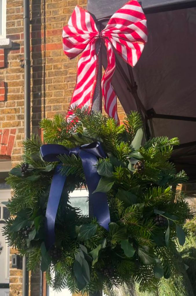 A handmade Christmas wreath of fir and holly with a navy ribbon
