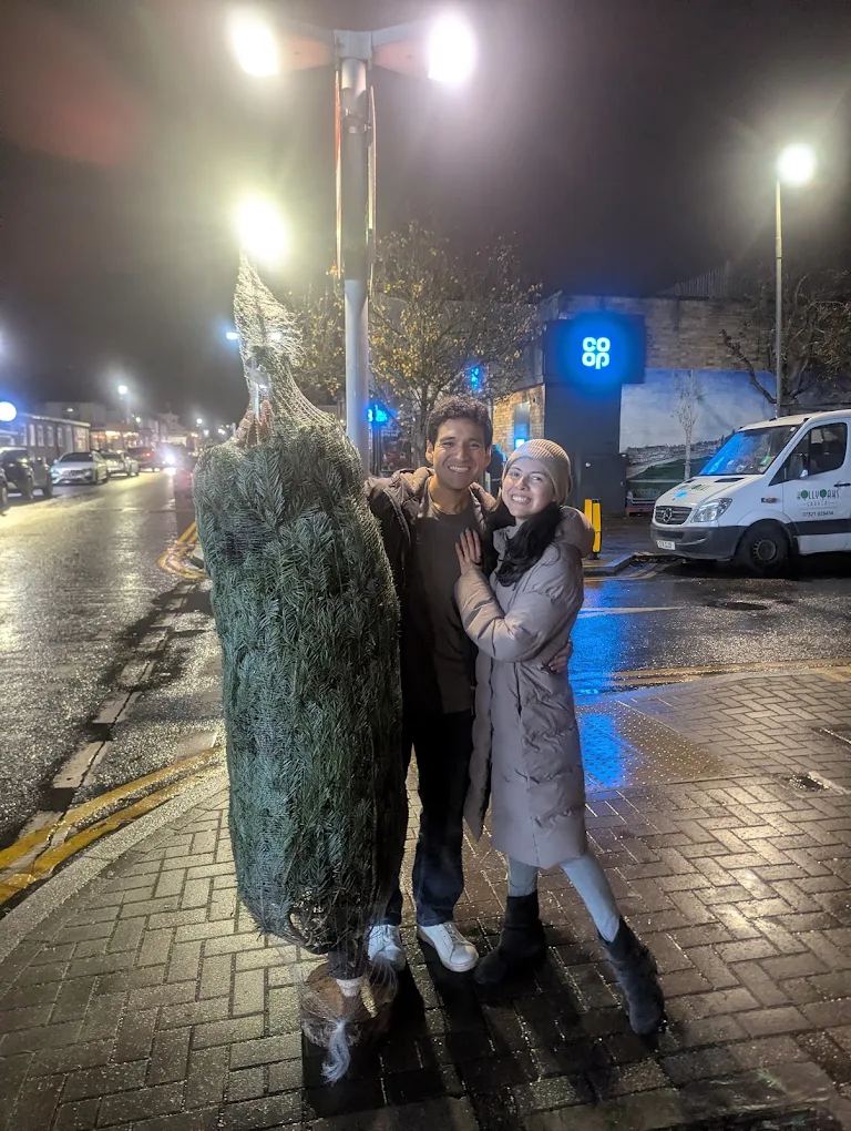 A couple with their netted Christmas tree on an evening pick-up, in front of the Co-op