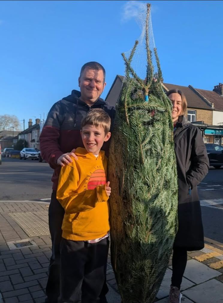 A smiling dad, mum and son with their freshly netted Nordmann fir on a sunny day