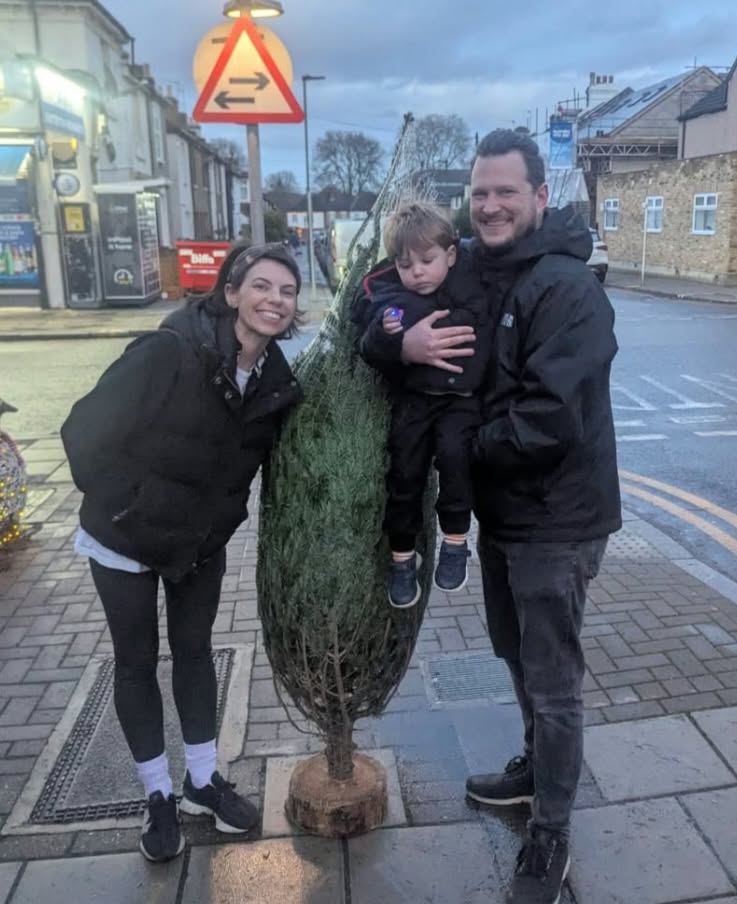 A couple and their toddler with their Christmas tree on the pavement